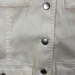 May include: White corduroy jacket with silver buttons. The buttons have a logo on them.