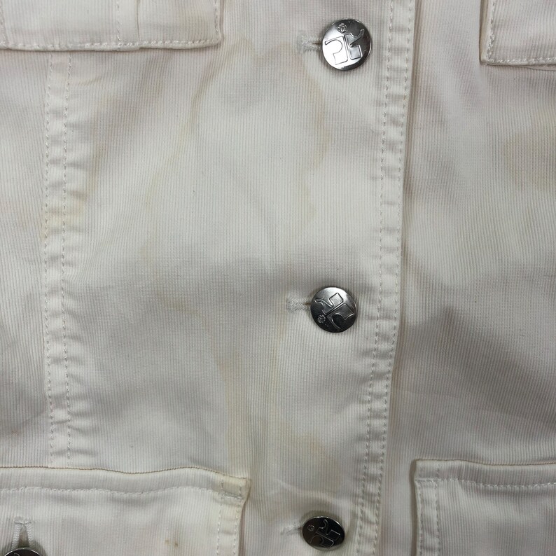 May include: White corduroy jacket with silver buttons. The buttons have a logo on them.