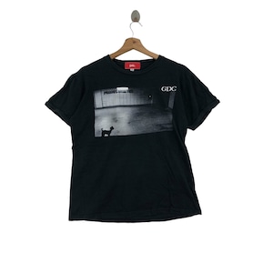 Puede incluir: Camiseta negra de manga corta con un estampado gráfico de un perro frente a un edificio con el texto "PERROS GUAU GUAU" y "GDC" en la parte delantera.