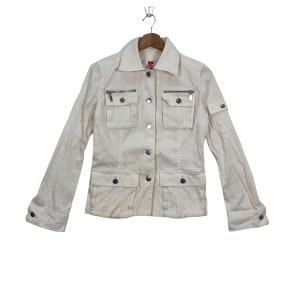 May include: A white denim jacket with a button-up front and multiple pockets. The jacket has silver zipper accents and a red logo on the left side of the chest.