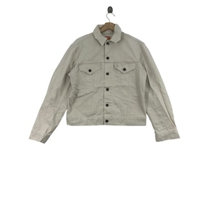 Op de afbeelding: Een lichtbeige denim jack met knoopsluiting en twee voorzakken.