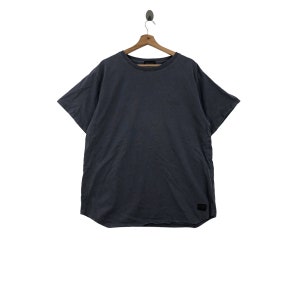 Puede incluir: Una camiseta lisa de color azul oscuro con mangas cortas y cuello redondo. La camiseta tiene una pequeña etiqueta negra en la parte inferior derecha.