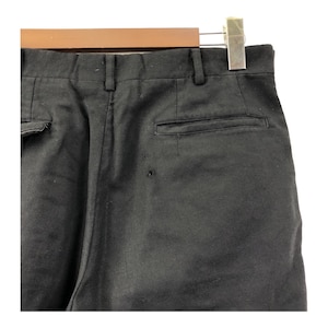 May include: Close-up of black pants hanging on a wooden hanger. The pants have a buttoned back pocket and a small hole near the pocket. The pants are made of a solid black fabric.