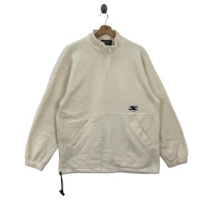 May include: A cream-coloured fleece pullover with a half-zip closure and a kangaroo pocket. The pullover has a small embroidered logo on the chest that says "Excel".