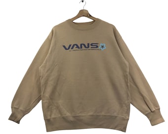 May include: A tan sweatshirt with a navy blue Vans logo and a blue and white star graphic. The text below the logo reads "Off The Wall".