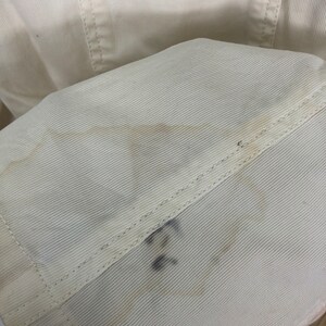 May include: Close-up of a white corduroy fabric with a subtle texture. The fabric has a faint yellow stain and a handwritten number "22" in black ink.