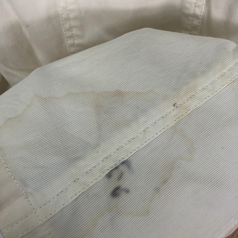May include: Close-up of a white corduroy fabric with a subtle texture. The fabric has a faint yellow stain and a handwritten number "22" in black ink.
