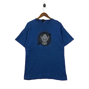 May include: Blue t-shirt with a graphic of an alien inside a circle with text. The alien is gray with large eyes and a small mouth. The text around the circle is in a dark gray color. The t-shirt is hanging on a wooden hanger.
