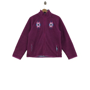 May include: A purple fleece jacket with a zip fastening and a geometric pattern on the front. The jacket has two pockets on the sides.