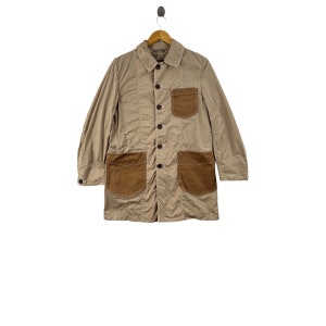 May include: A beige long-sleeved jacket with brown suede patch pockets. The jacket has a button-up front and a collared neckline.