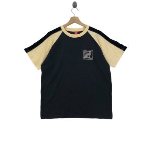 May include: A black and yellow short-sleeved t-shirt with a kangaroo graphic on the front. The shirt has a red tag on the collar.