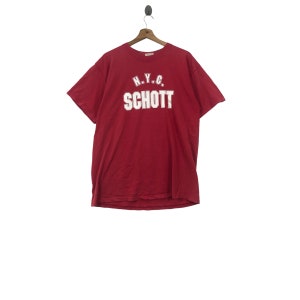 May include: Red short-sleeved t-shirt with white text that reads "N.Y.C. SCHOTT"