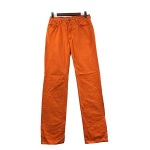 Op de afbeelding: Een oranje spijkerbroek met rechte pijpen, een knoopsluiting en riemlussen.