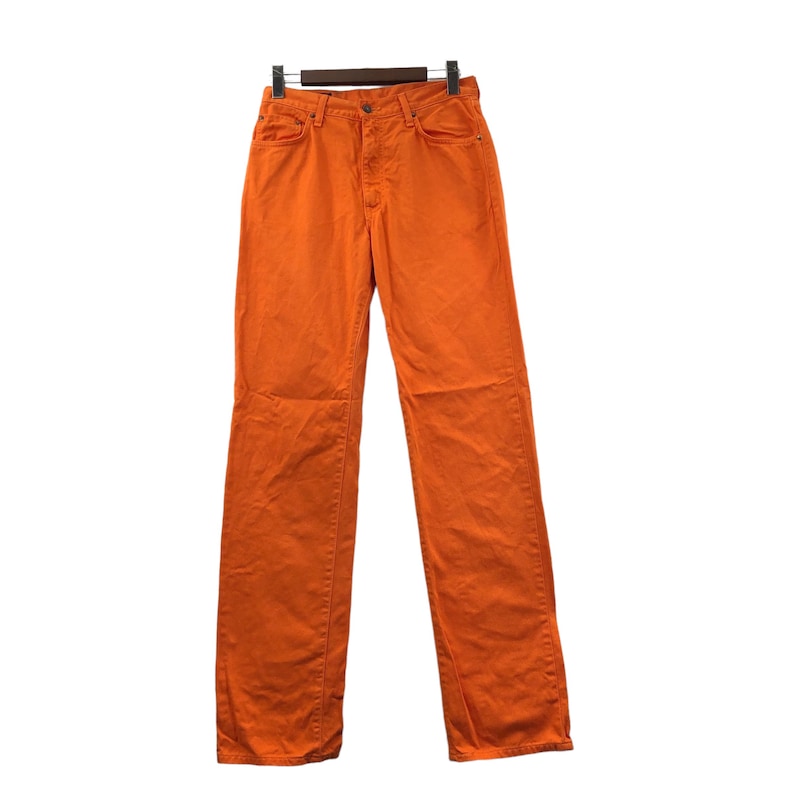 Op de afbeelding: Een oranje spijkerbroek met rechte pijpen, een knoopsluiting en riemlussen.