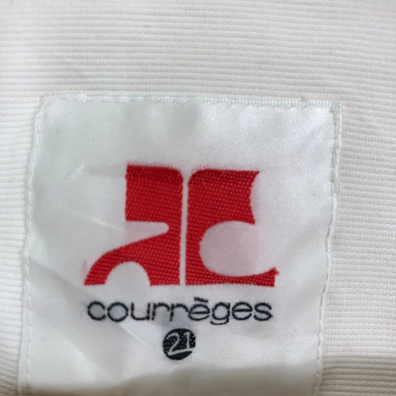 May include: White label with red "AC" logo and black text "Courr&egrave;ges" with a small circle containing the number "21" underneath.