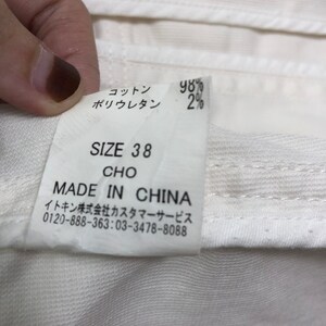 May include: White tag with black text indicating the size is 38, the material is 98% cotton and 2% polyurethane, and the item is made in China. The tag also includes contact information for customer service.