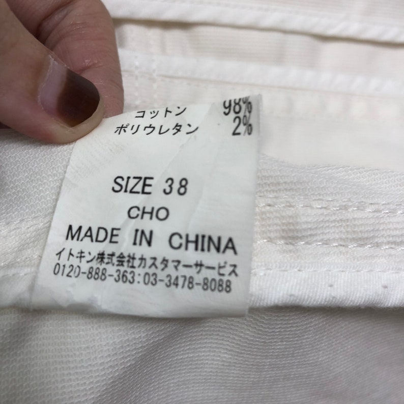May include: White tag with black text indicating the size is 38, the material is 98% cotton and 2% polyurethane, and the item is made in China. The tag also includes contact information for customer service.