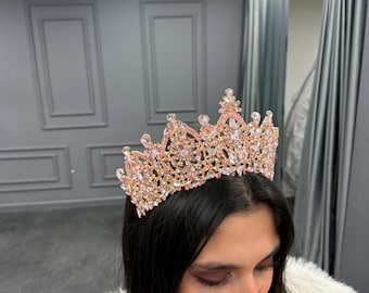 May include: A pink and gold crown with rhinestones. The crown is made of metal and has a delicate design.