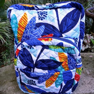 May include: A quilted backpack with a blue, white, yellow, and orange floral pattern. The backpack has a zipper closure and a top handle.