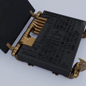 May include: A black book with gold hinges and decorative eagle-shaped clasps. The book is open and the pages are covered in hieroglyphics.