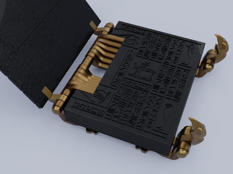 May include: A black book with gold hinges and decorative eagle-shaped clasps. The book is open and the pages are covered in hieroglyphics.