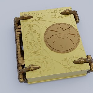 May include: A gold-colored book with intricate designs and a circular emblem featuring an eye and a symbol. The book has two clasps on each side.