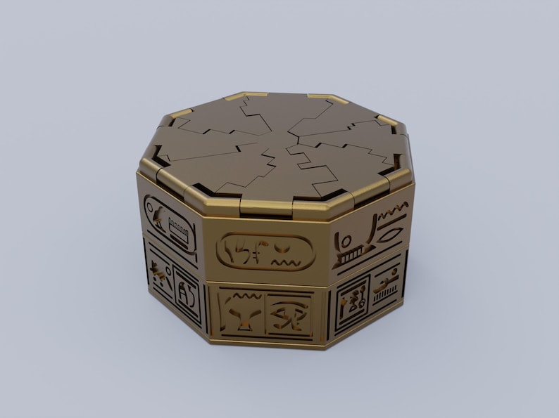 May include: A gold-colored octagonal box with intricate carvings and a hinged lid. The box is decorated with hieroglyphic-like symbols.