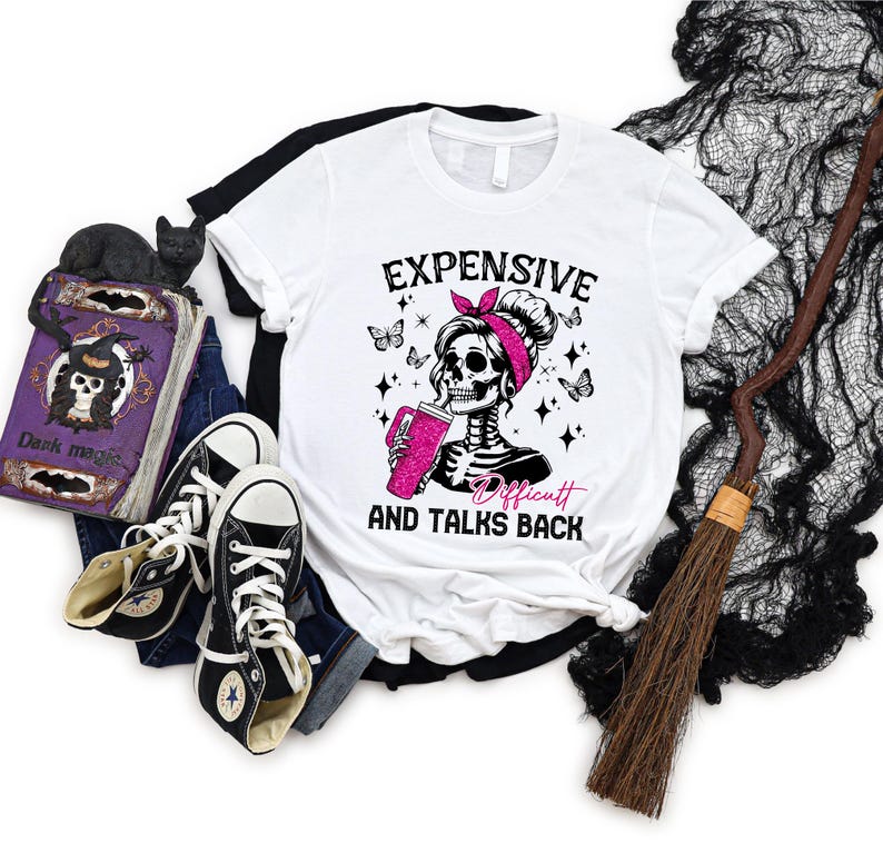 May include: White t-shirt with a black and white illustration of a skeleton woman with a pink bow in her hair. The skeleton is holding a pink cup and the text "Expensive and Talks Back" is printed below the illustration.