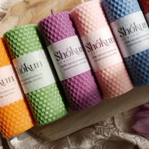 May include: Six honeycomb beeswax candles in various colors, including orange, green, purple, pink, and blue. Each candle has a label that reads "Shókun" and "100% natural beeswax handmade candles".
