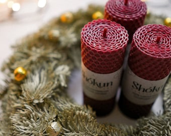 May include: Three red beeswax candles with gold bells and a green pine wreath. The candles are labeled "Shoko" and "Hokun".