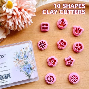 Op de afbeelding: Tien roze plastic klei-uitstekers in verschillende vormen, waaronder bloemen, sterren en een vierkant. De uitstekers zijn gerangschikt op een roze oppervlak. De tekst "10 SHAPES CLAY CUTTERS" is in het zwart bovenaan de afbeelding gedrukt.