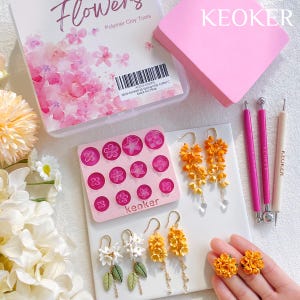 Könnte beinhalten: Ein Set aus Polymer Clay-Werkzeugen zum Herstellen von Blumen, darunter eine rosa Form mit verschiedenen Blumenformen, eine rosa und weiße Box mit dem Text "Flowers Polymer Clay Tools", zwei rosa und weiße Werkzeuge und ein Paar Ohrringe mit orangefarbenen und weißen Blumen.