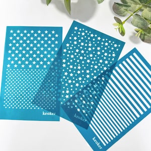 May include: Three blue plastic stencils with white star and stripe patterns. The stencils are labeled "keoker" in white text.