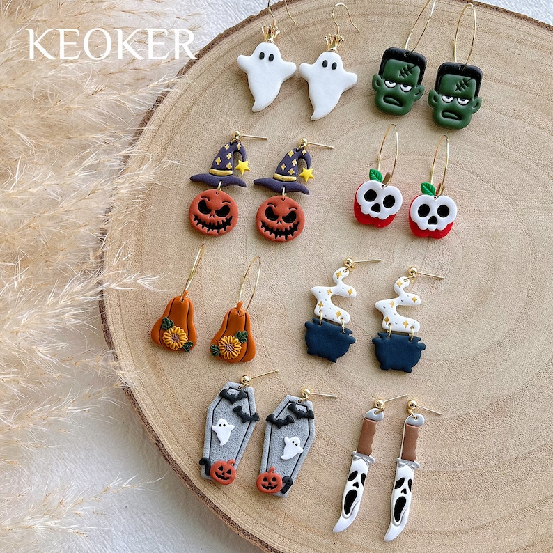 May include: A collection of Halloween-themed earrings. Designs include ghosts, Frankenstein's monster, jack-o'-lanterns, apples with skulls, pumpkins, cauldrons with smoke, coffins with ghosts, and knives with ghost faces. The earrings are on gold hoops.