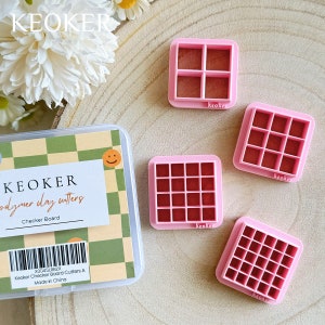 Peut inclure: Quatre emporte-pièces en plastique rose en forme de damier avec un intérieur rouge. Les emporte-pièces sont de tailles différentes et sont posés sur une surface en bois. Le plus grand emporte-pièce a 25 carrés, le suivant a 16 carrés, le suivant a 9 carrés et le plus petit a 4 carrés. Les emporte-pièces sont étiquetés "keoker".