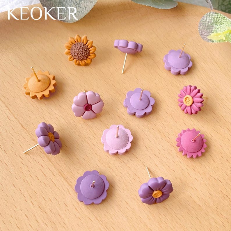 Pode incluir: Conjunto de brincos coloridos em forma de flor com postes dourados. Os brincos s&atilde;o em tons de roxo, rosa e laranja. Os brincos est&atilde;o dispostos sobre uma superf&iacute;cie de madeira.