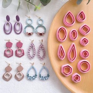 Puede incluir: Una colección de pendientes hechos a mano en varias formas y colores, incluyendo morado, rosa y azul. Los pendientes presentan diseños geométricos, detalles florales y elementos en capas. También se muestran cortadores de arcilla polimérica rosa en varias formas, incluyendo gotas, óvalos y hexágonos.