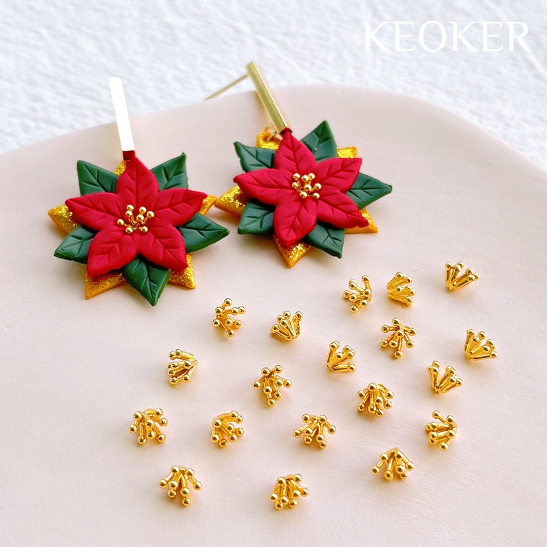 May include: A pair of gold earrings with red and green poinsettia flower charms. The earrings are surrounded by 16 gold flower-shaped earring backs.