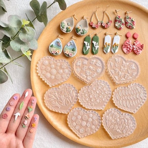 以下が含まれることがあります： イヤリングを作るための透明なハート型のシリコンモールドのセット。モールドは、さまざまな花や葉のデザインが施されています。また、花や葉のデザインが施された手作りポリマークレイのイヤリングもいくつかあります。