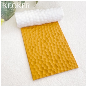 Puede incluir: Un rodillo de silicona amarillo con un patrón de panal. El rodillo se utiliza para crear textura en fondant u otros materiales comestibles.