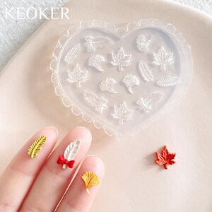 May include: A heart-shaped silicone mold with 12 different leaf designs. The mold is clear and has a scalloped edge. There are also several small, colorful resin leaves on a white surface.