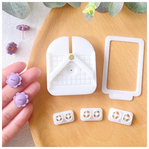 May include: A set of white plastic molds for making resin earrings. The molds are shaped like a flower and have different sizes labeled S, M, and L. There are also two white plastic tools for making the earrings.