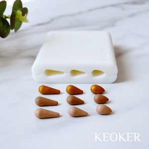 Puede incluir: Un molde de silicona blanco con cuatro cavidades en forma de lágrima. El molde está etiquetado con "KEOKER". Hay nueve piezas de arcilla polimérica en forma de lágrima en varios tonos de marrón y dorado.