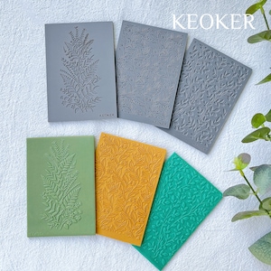 May include: Six silicone stamps with floral designs. The stamps are in various colors, including gray, green, and yellow. The stamps are arranged in a row on a white surface. The word "KEOKER" is printed on the stamps.