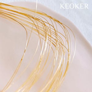 May include: A close-up of a bundle of thin, gold-colored wire. The wire is arranged in a curved pattern, creating a soft, flowing look.