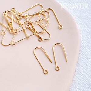 Peut inclure: Gros plan sur un tas de crochets d'oreille dor&eacute;s. Les crochets sont en m&eacute;tal et ont un design simple et &eacute;l&eacute;gant. Deux crochets sont s&eacute;par&eacute;s du tas, montrant la forme et la taille des crochets.