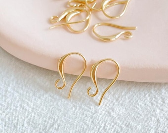 May include: Gold-toned earring hooks, also known as ear wires, are shown on a pink surface. The hooks are made of metal and have a smooth, polished finish.