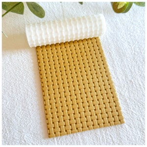 Puede incluir: Un rodillo de silicona texturizado marrón con un patrón tejido. El rodillo está enrollado sobre una hoja del mismo material.