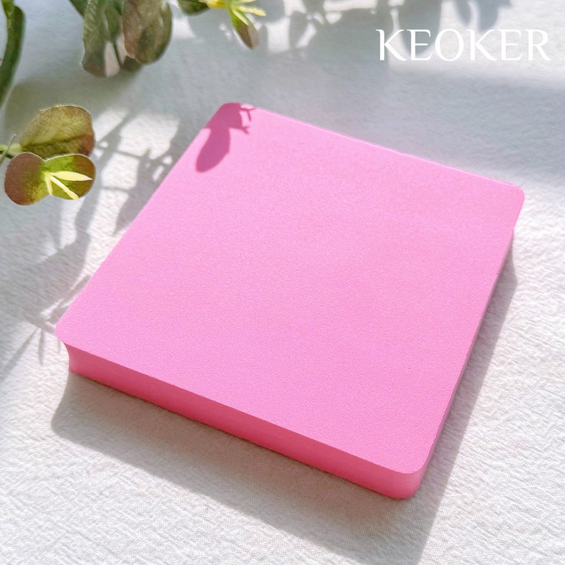 May include: A pink square sticky note pad with the word "KEOKER" printed in white on the top right corner.