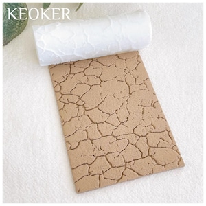 Könnte beinhalten: Eine weiße Silikon-Rollrolle mit einem Rissmuster. Die Rollrolle liegt auf einer braunen Silikonmatte mit einem Rissmuster. Die Matte wird verwendet, um eine Rissstruktur auf Fondant oder anderen essbaren Materialien zu erzeugen.